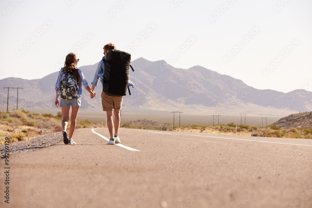 Rear View Of Couple On Vacation Hitchhiking Along Road Rear View Of Couple On Vacation Hitchhiking Along Road