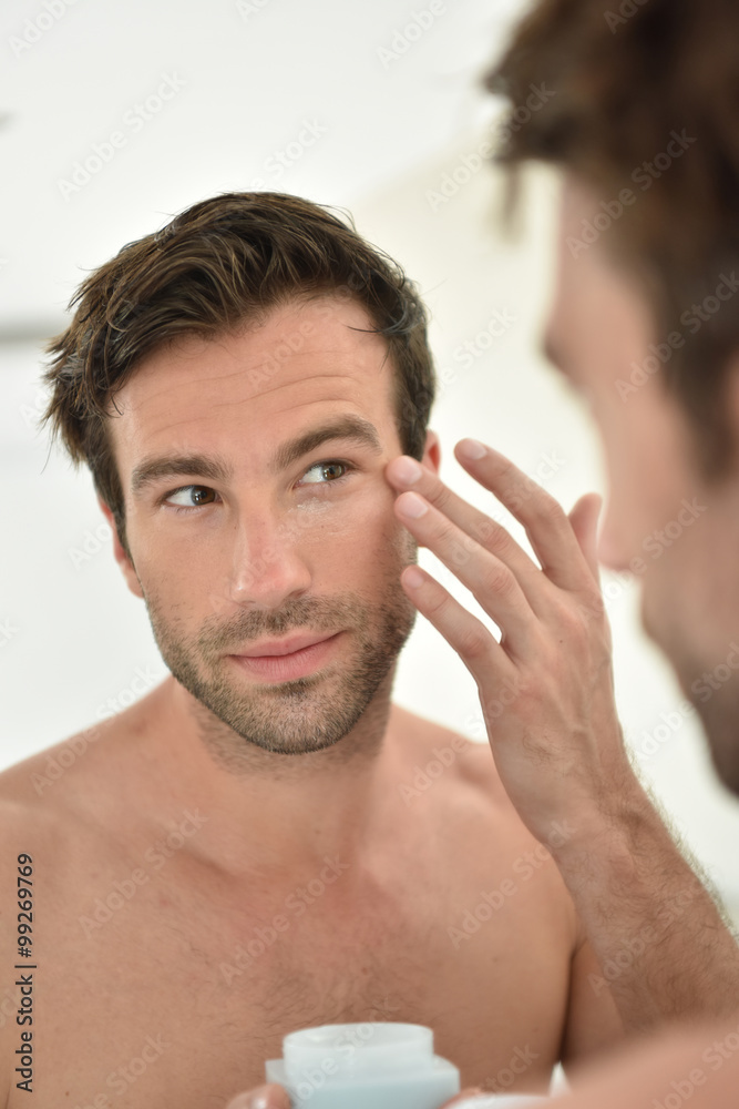 Obraz premium Handsome man applying facial cream in front of mirror