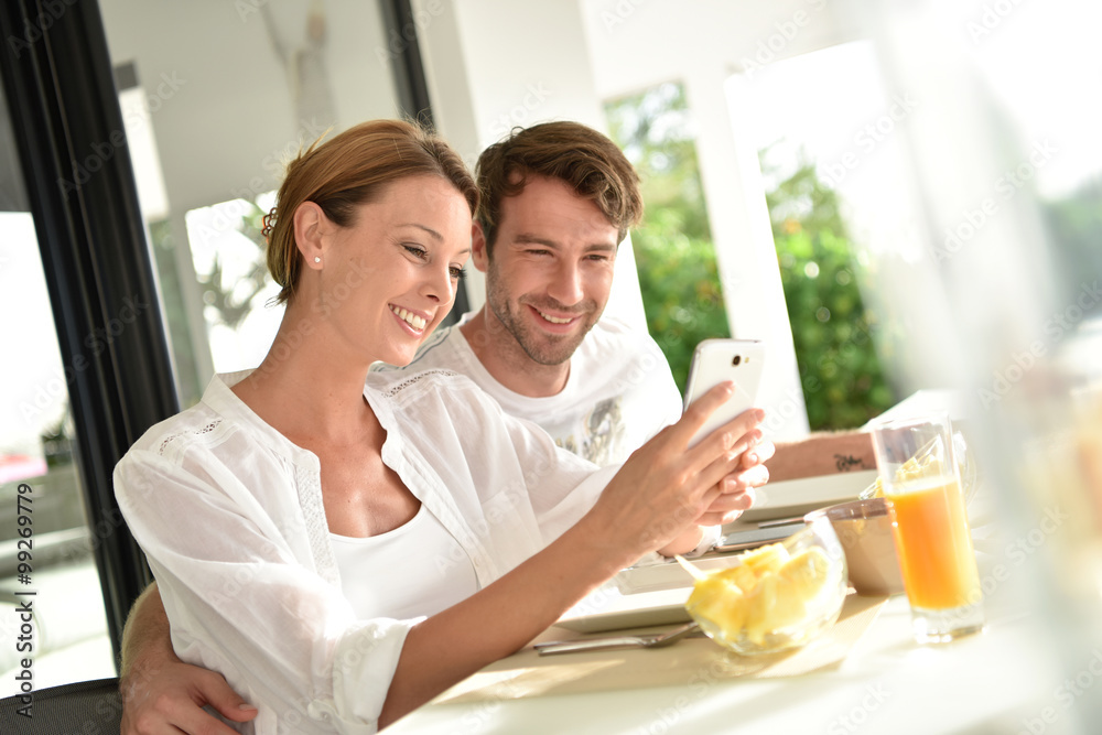 Couple having fun using smartphone at breakfast time Couple having fun using smartphone at breakfast time
