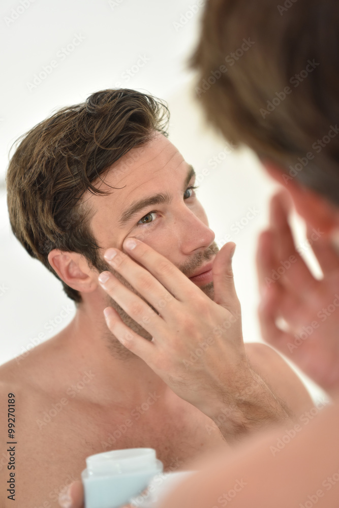 Handsome man applying facial cream in front of mirror Handsome man applying facial cream in front of mirror