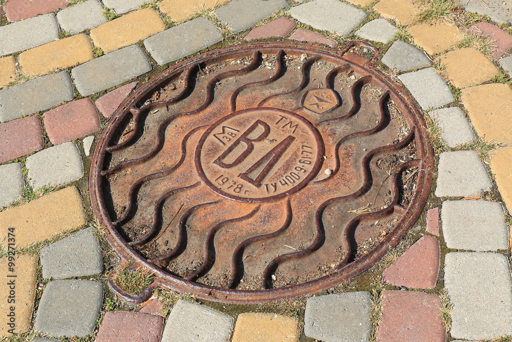 Rusted manhole on a street with pavement from multicolor block