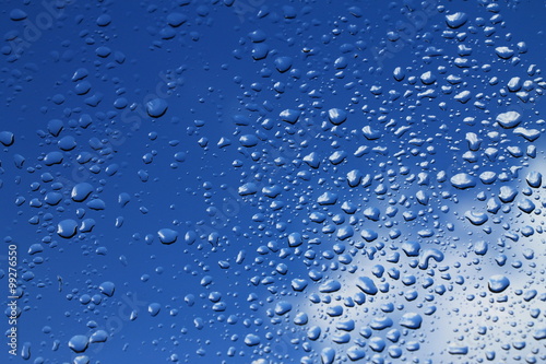 Rain drops on window with blue cloudy sky in background