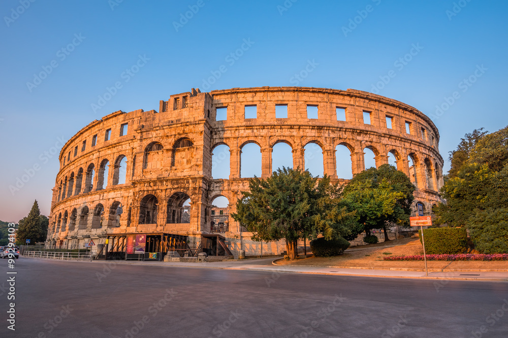 Ancient Roman Amphitheater in Pula, Croatia, Famous Travel Destination, in Sunny Summer Evening with Trees and Flowers in Foreground