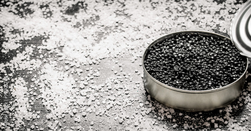 Black caviar in a jar with salt . On black wooden table.