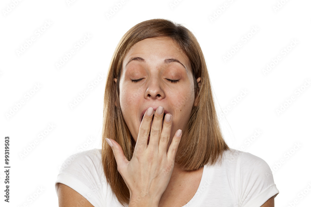 sleepy young woman yawns and covers her mouth with a hand sleepy young woman yawns and covers her mouth with a hand