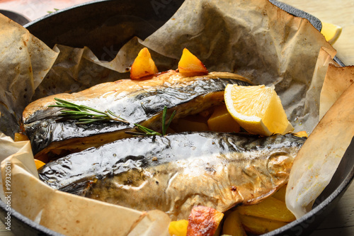 Baked fish mackerel with baked potato in a pan, rosemary, lemon and spice on a wooden background photo