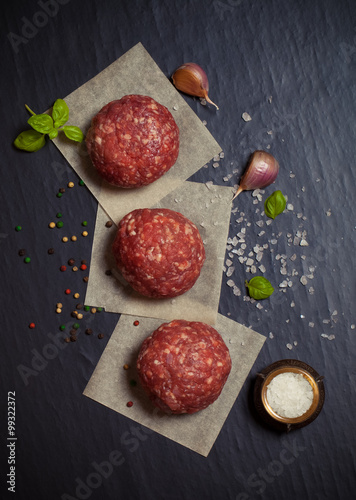 Foto Raw ground beef meat steak cutlets with herbs and spices on blac