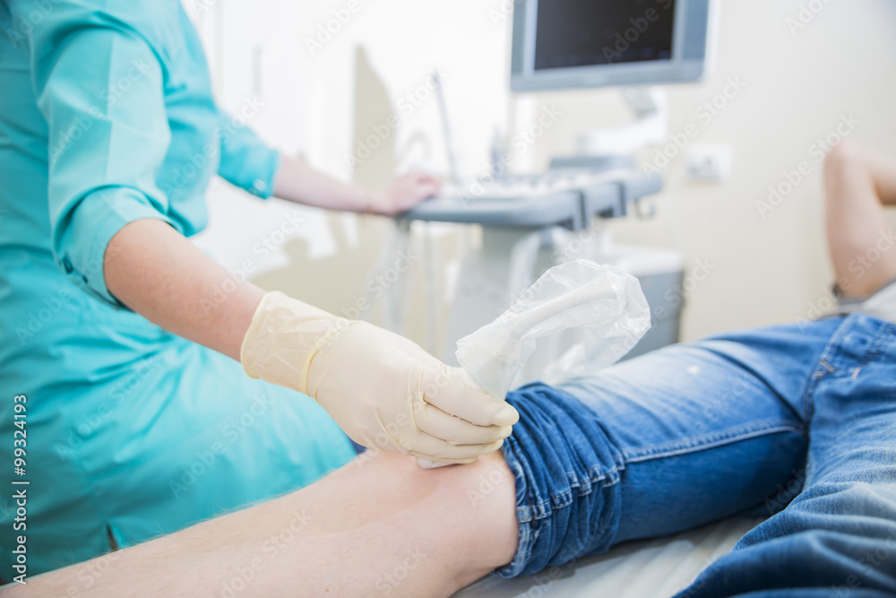 closeup hand of woman doctor doing an ultrasound looks at the leg and knee of the patient in the medical center