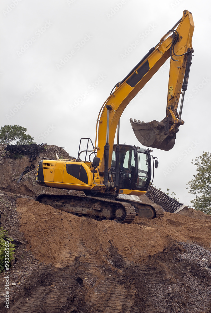 heavy yellow excavator with shovel standing on hill