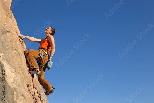 Young male climber hanging by a cliff.