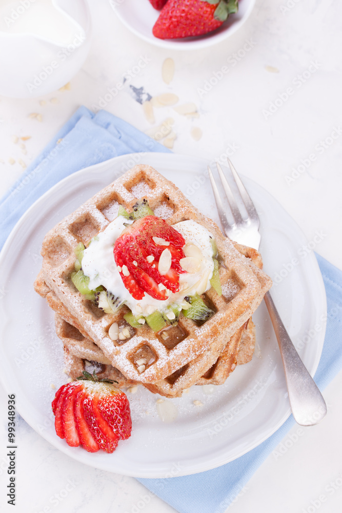 Waffles with wholewheat flour and fruits on a white plate on a blue napkin, top view.. Waffles with wholewheat flour and fruits on a white plate on a blue napkin, top view..