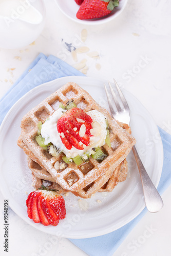 Waffles with wholewheat flour and fruits on a white plate on a blue napkin, top view..