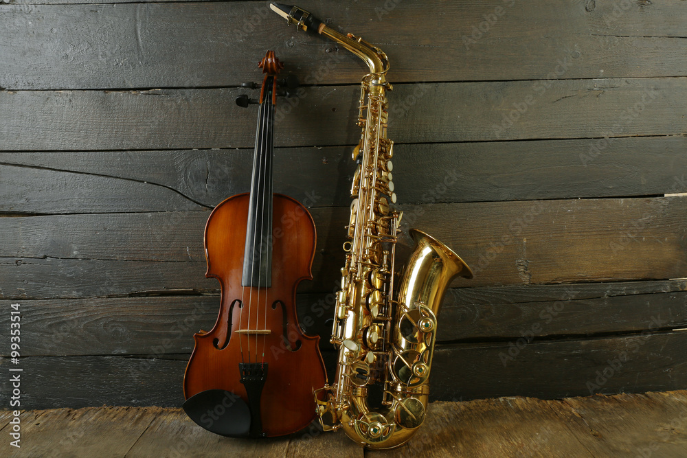 Naklejka premium Beautiful golden saxophone with violin on wooden background