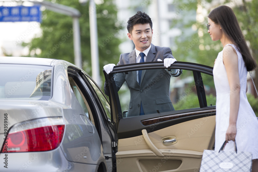 Naklejka premium Chauffeur opening car door for a young woman