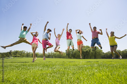 Cheerful young adults jumping on grass