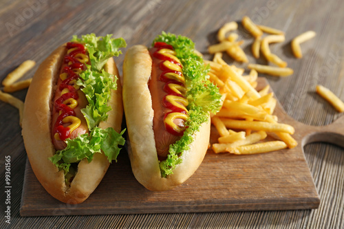 Delicious hot-dogs with French fries on wooden chopping board