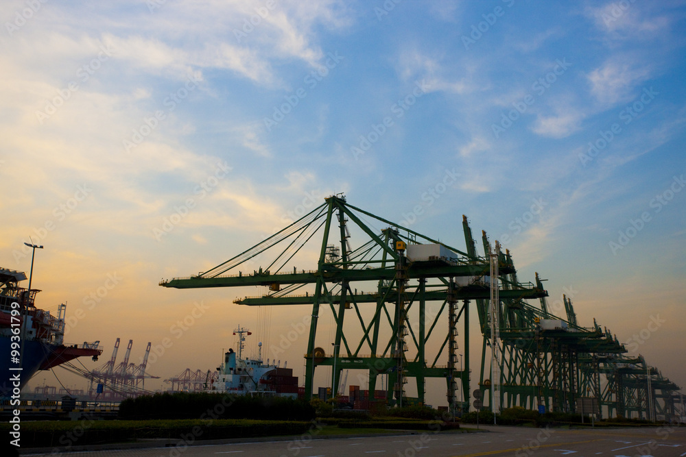 View of cranes and cargo ships at dusk