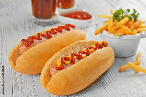 Delicious hot-dog with French fries and vegetables on white wooden table