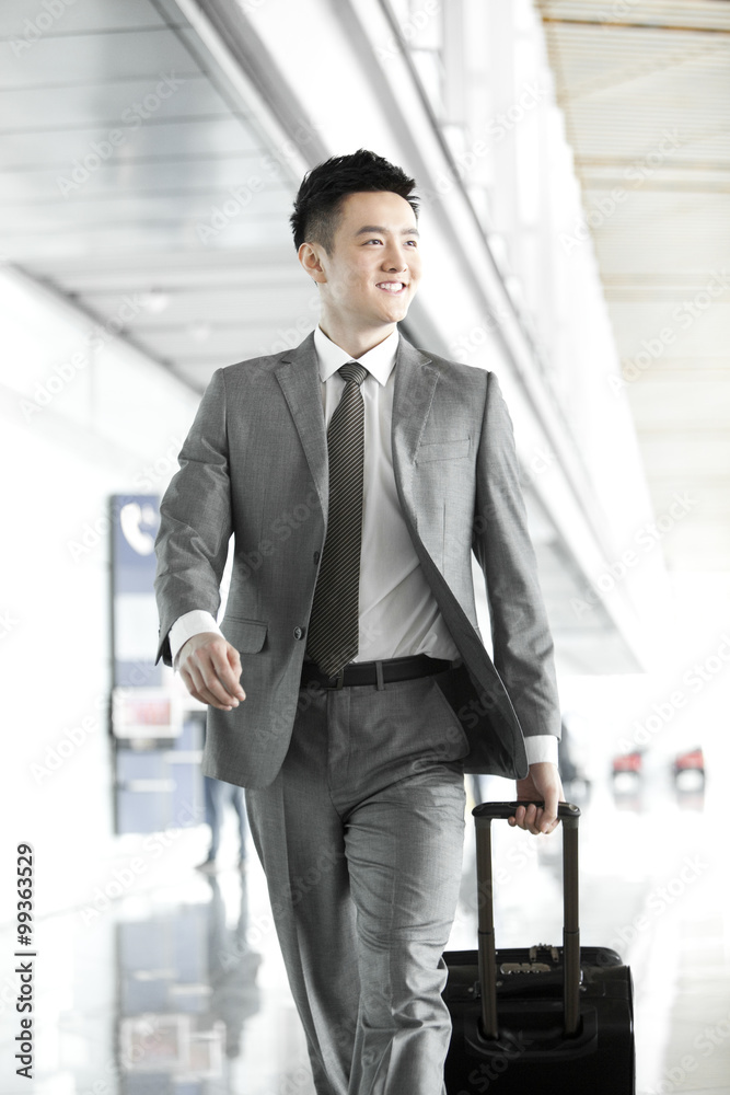 Businessman pulling wheeled luggage in airport lobby Businessman pulling wheeled luggage in airport lobby