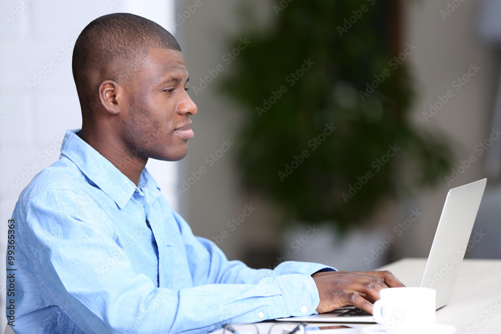 African American businessman in blue shirt working on laptop, close up African American businessman in blue shirt working on laptop, close up