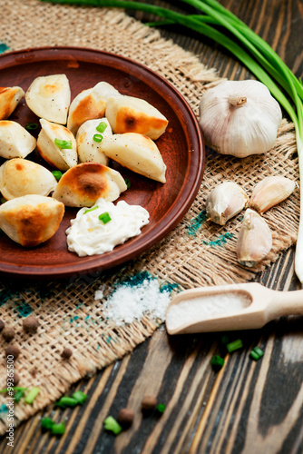 Ukrainian and china national cuisine , fried dumplings with meat or potatoes with sour cream or mayonnaise , green onions, garlic , pepper and spices on a wooden background