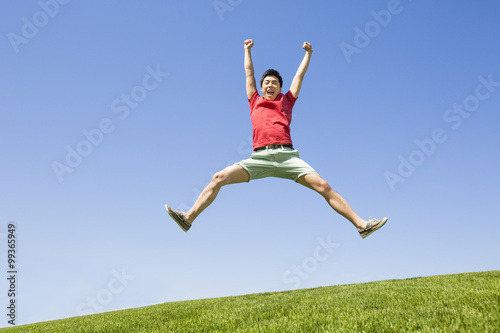 Cheerful young man jumping on grass