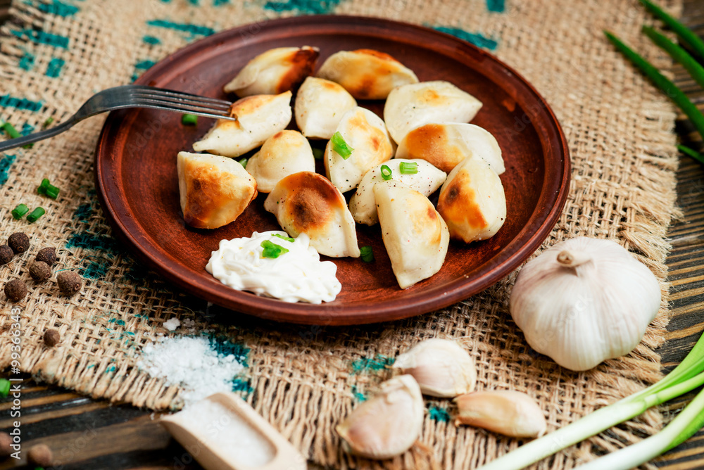 Ukrainian and china national cuisine , fried dumplings with meat or potatoes with sour cream or mayonnaise , green onions, garlic , pepper and spices on a wooden background Ukrainian and china national cuisine , fried dumplings with meat or potatoes with sour cream or mayonnaise , green onions, garlic , pepper and spices on a wooden background