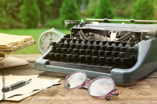 Obraz na plátně Vintage black typewriter with papers and pen on wooden table, outdoors