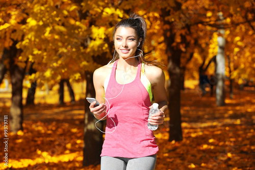 Fototapeta Naklejka Na Ścianę i Meble -  Young beautiful woman with bottle of water running in autumn park and listening to music with headphones.