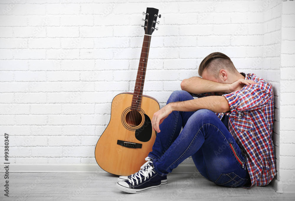 Fototapeta premium Young musician with guitar on light wall background