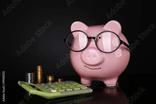 Piggy bank in glasses with calculator and coins on dark background