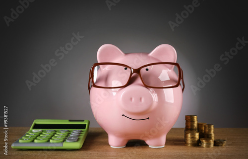 Piggy bank in glasses with calculator and coins on grey background
