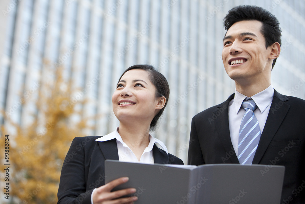 A businessman and businesswoman outside office buildings with a document A businessman and businesswoman outside office buildings with a document