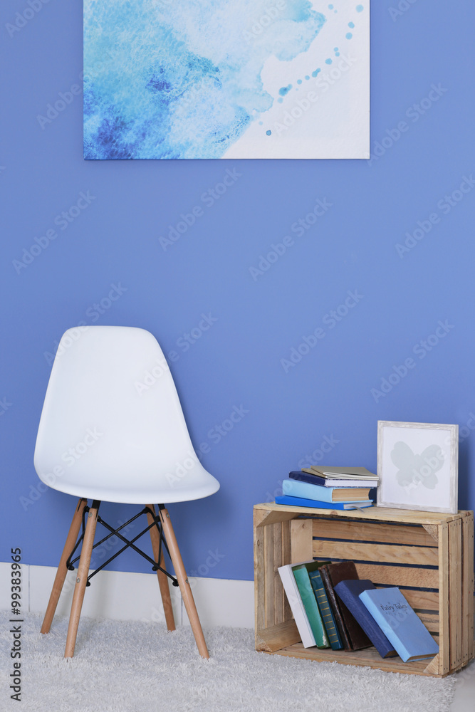 Fototapeta premium Room design with white chair, bookcase and picture over blue wall