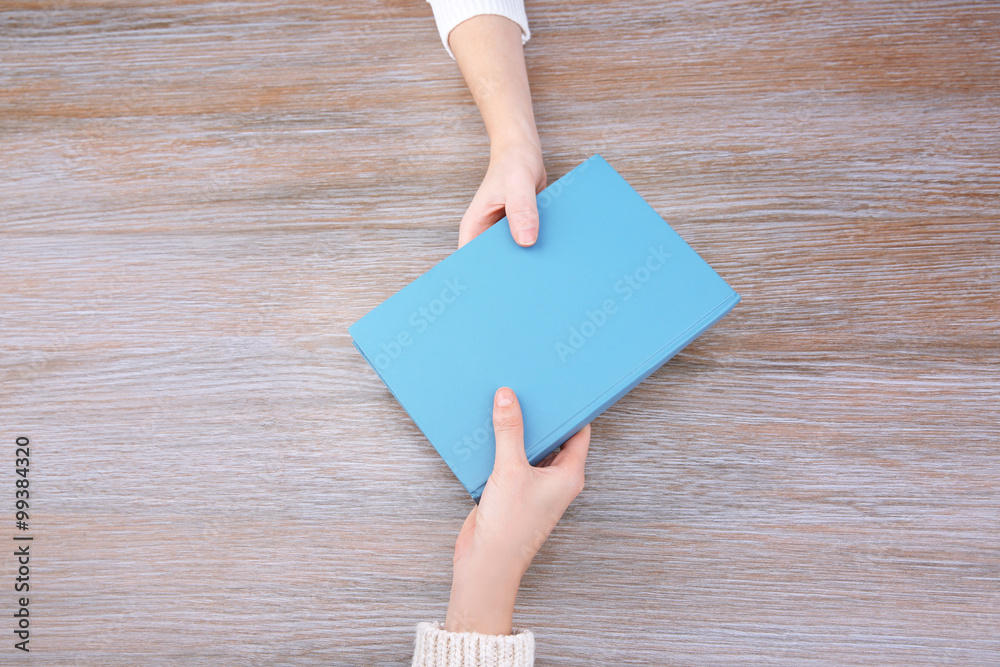 Woman giving book to woman, on wooden table background Woman giving book to woman, on wooden table background