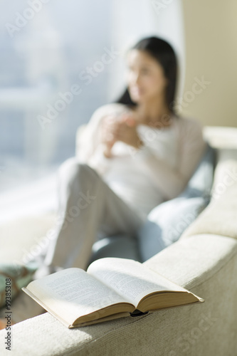 Happy young woman sitting on sofa with a book