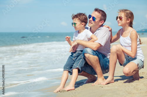 Father and children sitting on the beach at the day time.