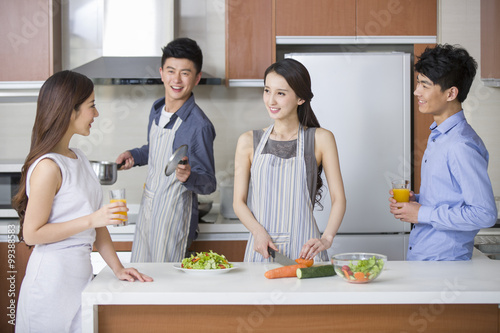 Young couple cooking and talking with their friends in the kitchen
