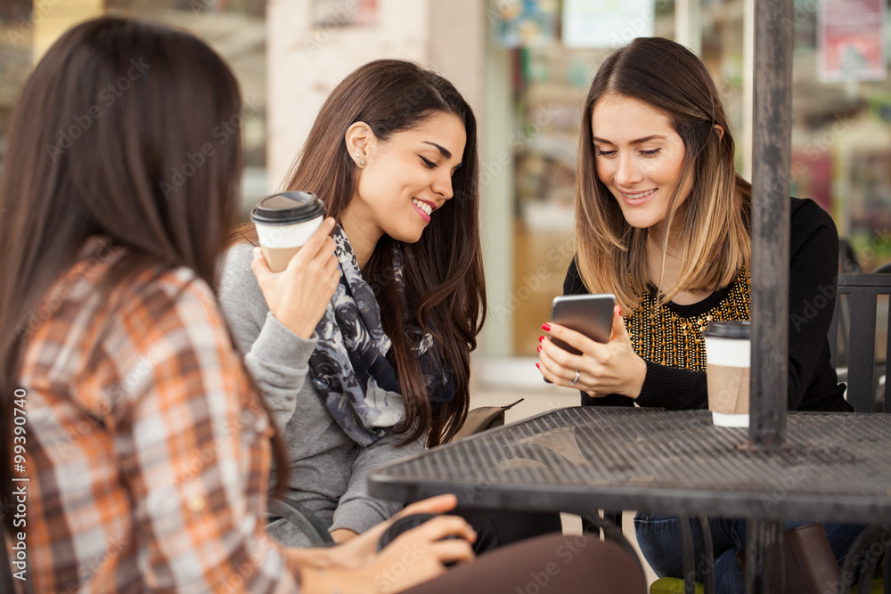 Female friends looking at a smartphone while sitting in a coffee shop Female friends looking at a smartphone while sitting in a coffee shop