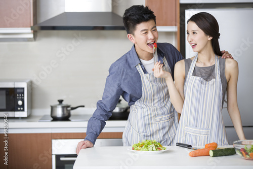 Young woman feeding boyfriend tomato in the kitchen