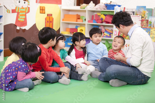 Male teacher sitting on floor with cute kindergarten children