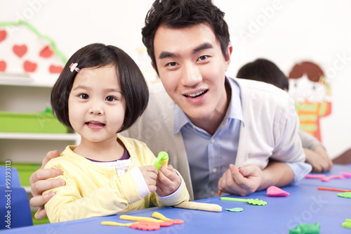 Kindergarten teacher and lovely girl playing with child's play clay