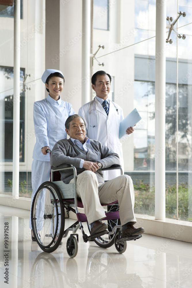 Nurse Pushes Senior Man in a Wheelchair, Doctor Walks Alongside