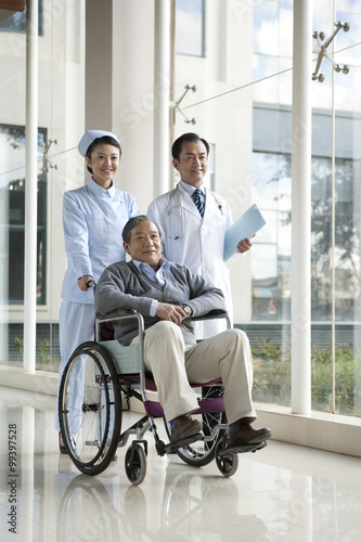 Nurse Pushes Senior Man in a Wheelchair, Doctor Walks Alongside