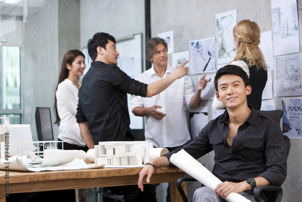 Architect holding blueprint with his team in background Architect holding blueprint with his team in background