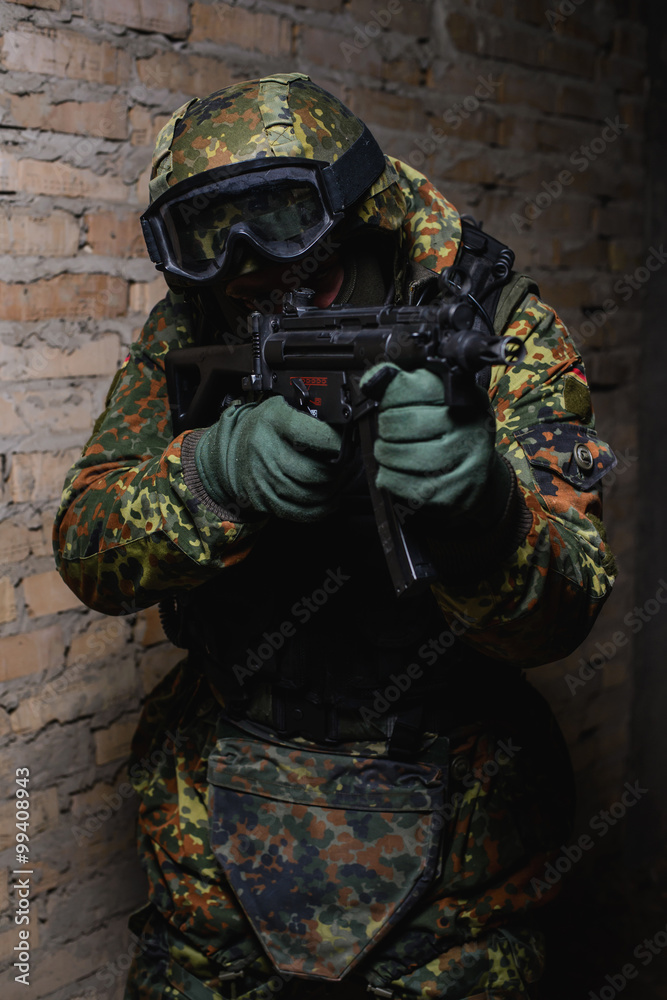 Fototapeta premium Armed man in helmet and body armor/ Armed man in helmet, body armor, mask, with weapon in hand takes aim at target