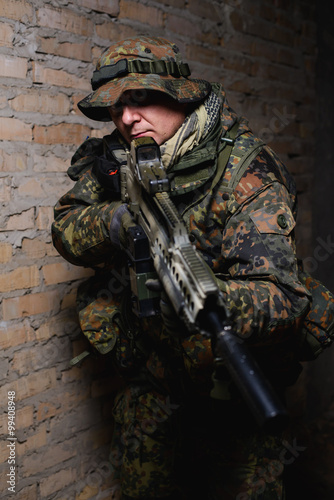 Foto Armed man with automatic rifle with silencer/Man in German uniform standing in d