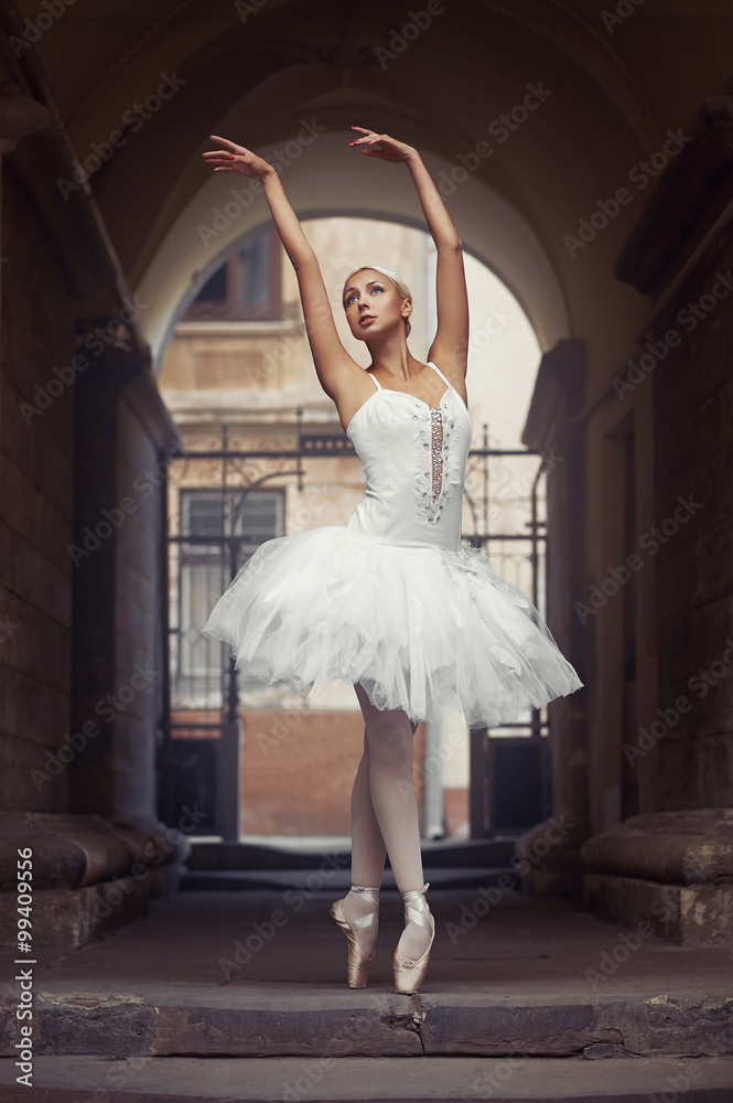 Fototapeta premium Looks like she is going to fly. Beautiful young female ballet dancer practicing her poses in an archway outdoors soft focus