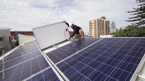 Solar technician installing solar panels on house roof.
