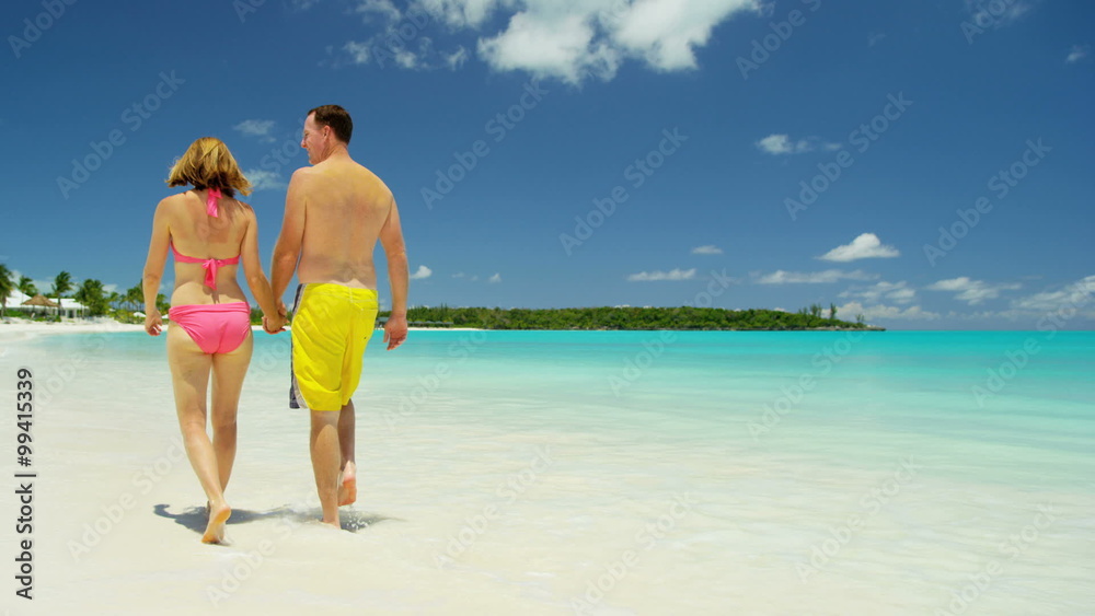 Barefoot Caucasian couple in swimwear holding hands on a tropical beach Barefoot Caucasian couple in swimwear holding hands on a tropical beach